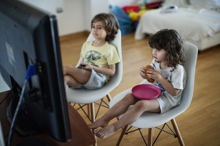 Crianças sentadas em frente à TV, comendo um lanche