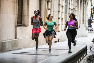 Três mulheres correndo em calçada com roupas esportivas