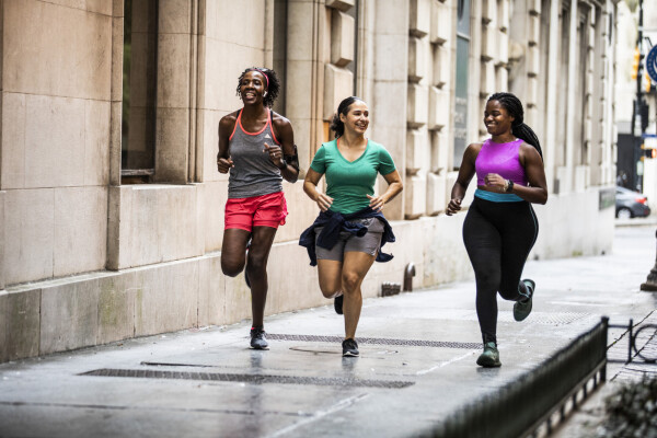 Três mulheres correndo em calçada com roupas esportivas