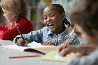 Criança sorrindo desenhando em um caderno na escola