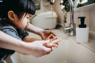 Criança com as mãos embaixo da torneira enquanto adulto toca suas mãos