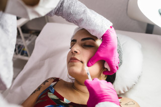 mulher deitada com o rosto sendo aplicado botox