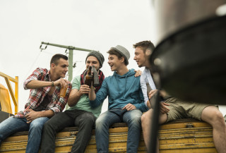 Grupo de amigos homens sentado em banco de madeira com garrafa de cerveja na mão