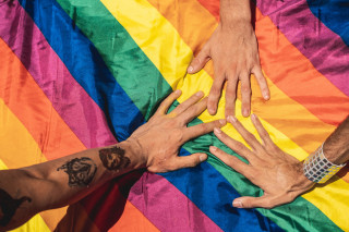Três mãos tocando uma bandeira LGBTQIAP+