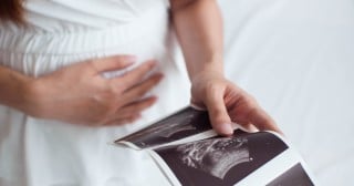 Mulher grávida segurando papel com imagem do resultado de ultrassom