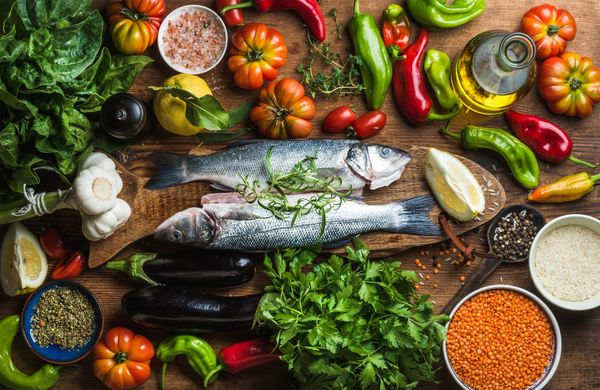 mesa com vários ingredientes, temperos, legumes e peixes