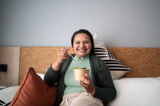 mulher sentada na cama enquanto come um pote de salada