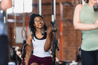 Mulher negra com deficiência sorrindo na academia levantando peso