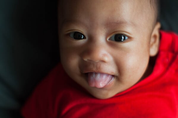 Bebê asiático veste blusa vermelha e mostra a linguinha