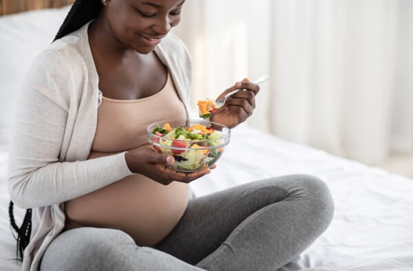 Mulher grávida sentada na cama e comendo uma salada