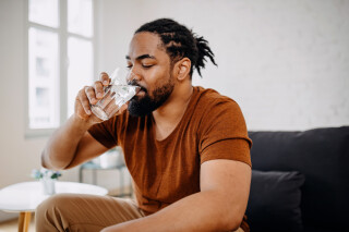 Homem negro sentado no sofá bebendo copo d'água