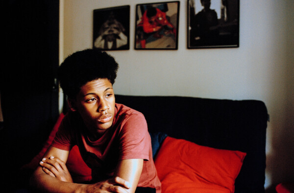 Jovem adolescente sentado em sofá preto com os braços cruzados