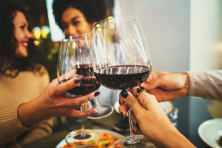 Foto aproximada de grupo de quatro amigos brindando com taças de vinho tinto