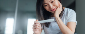 Mulher sentada na cama olhando para um teste de gravidez