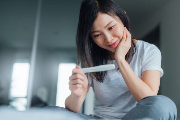 Mulher sentada na cama olhando para um teste de gravidez