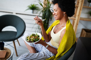 Mulher sorrindo sentada em cadeira com prato de legumes na mão