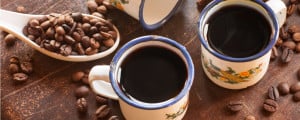 Duas xícaras cheias de café sobre uma mesa de madeira com uma colher cheia de grão de café