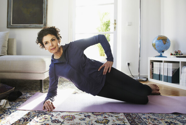 Mulher fazendo exercício de yoga em tapete, na sala de uma casa