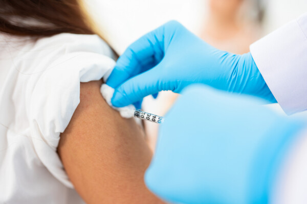 Foto aproximada de enfermeira aplicando vacina no braço de uma menina