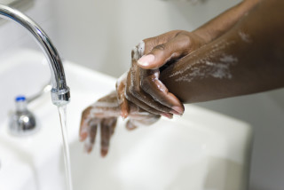 Imagem aproximada de médica, com pele negra, lavando as mãos com água e sabão