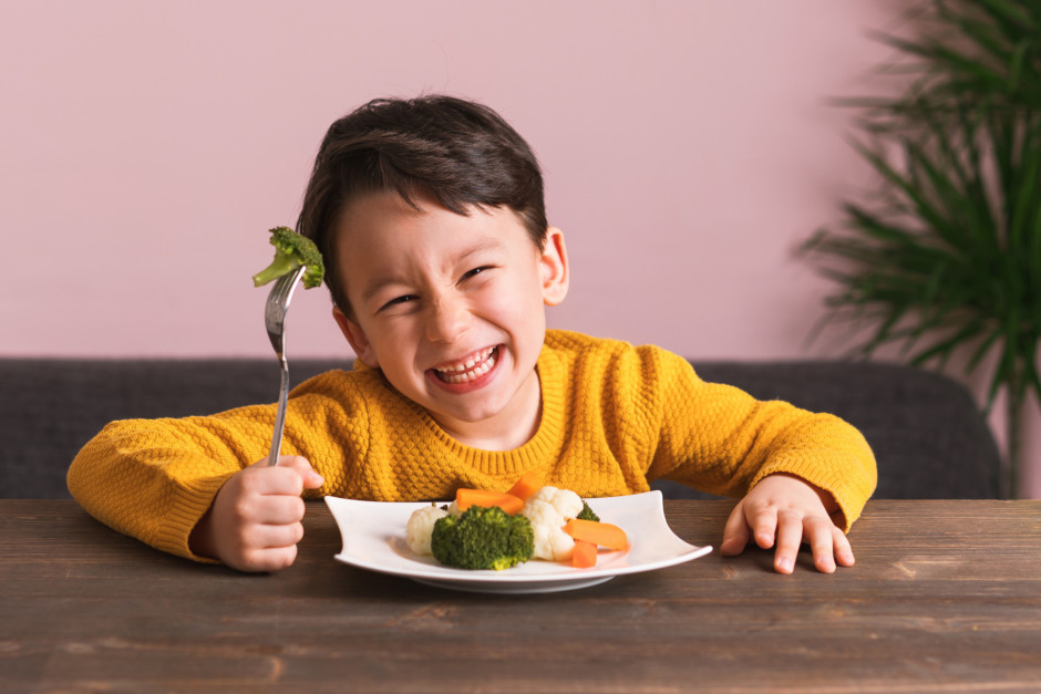 Criança sorrindo enquanto come prato com legumes