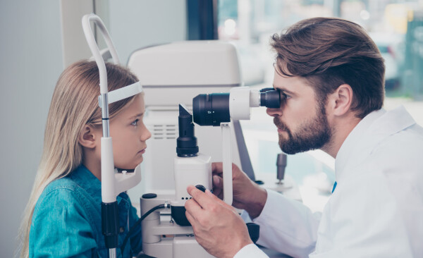 Menina de aproximadamente 8 anos faz exame oftalmológico com médico oftalmologista