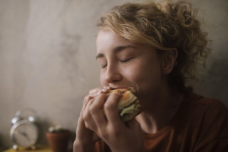 Mulher loira comendo um hambúrguer de olhos fechados
