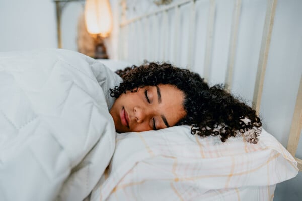 Adolescente de cabelos cacheados e pretos dormindo em uma cama com lençóis e cobertores brancos