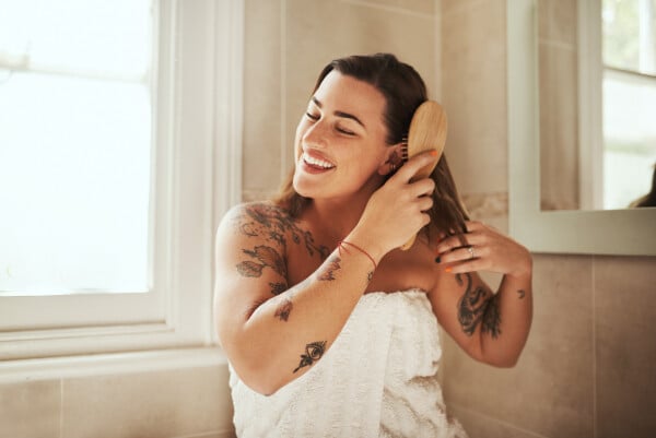 Mulher sorridente escovando o cabelo no banheiro