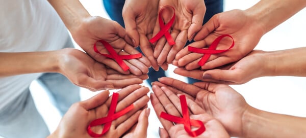 Diversas mãos seguram laços vermelhos, simbolizando o Dezembro Vermelho, campanha de prevenção ao HIV e outras Infecções Sexualmente Transmissíveis