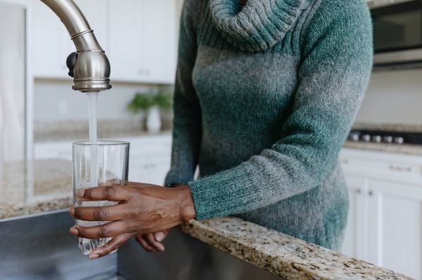 Mulher enchendo um copo de água da torneira
