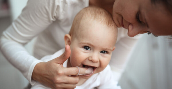 Mãe escovando os dentes do bebê com o dedo
