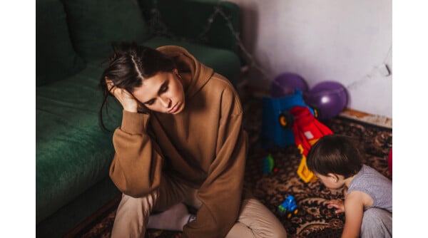 Mãe cansada com a mão na cabeça enquanto sua filha pequena brinca ao seu lado