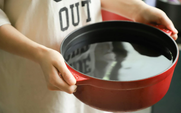 Imagem aproximada de mãos segurando panela com água