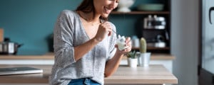 Mulher sorrindo enquanto come iogurte sentada na cozinha.