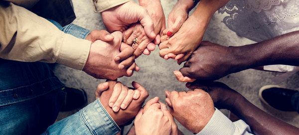 Pessoas de diversas etnias apertam as mãos uns dos outros, formando um círculo