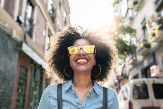Mulher sorrindo enquanto caminha pela cidade com um óculos de sol