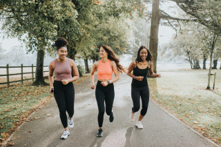 Três mulheres em roupas esportivas correndo na trilha de um parque