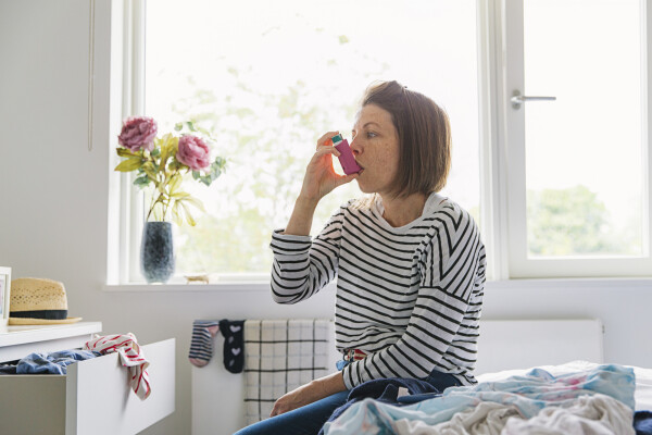 Mulher sentada na cama com uma bombinha de asma