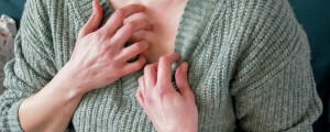 mulher coçando o peito com as unhas enquanto puxa um pouco a blusa verde para baixo