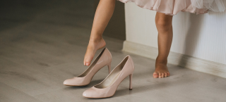 Menina de aproximadamente cinco anos coloca o pé dentro de um sapato de salto alto