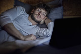 homem deitado na cama no escuro olhando para a tela de um notebook