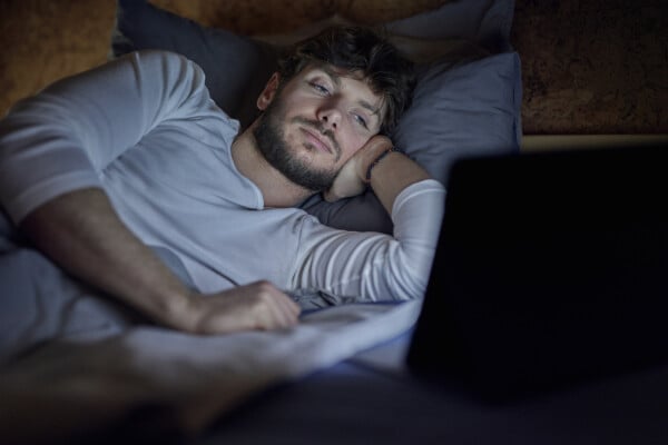 homem deitado na cama no escuro olhando para a tela de um notebook
