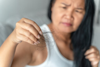 Mulher desfocada olhando para fios de cabelo que estão em sua mão, que está focada em primeiro plano