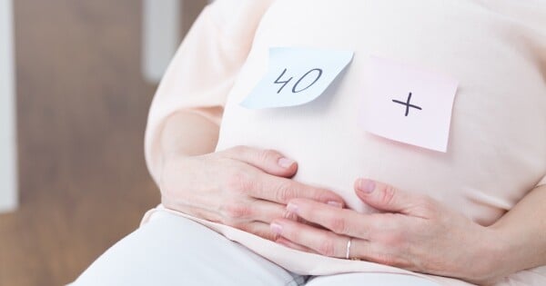 Mulher grávida com post its colados na barriga com os dizeres "40+"