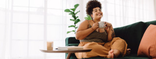 Mulher sentada no sofá sorrindo e tomando uma xícara de chá