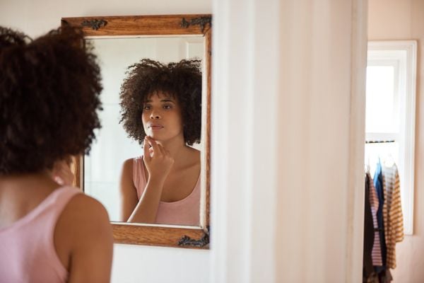 Mulher jovem olhando a pele no espelho