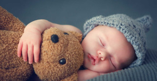 Bebê dormindo de lado abraçado a um urso de pelúcia