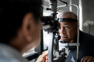 Na imagem, um homem negro de meia idade passa por exames oftalmológicos em um aparelho.
