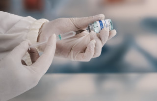 Imagem aproximada de mãos com luvas inserindo a vacina da COVID-19 em uma seringa